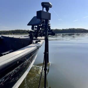 A close-up of a boat on a calm lake shows Garmin electronics and a Wireless Transducer Pole - First Mate XT (Formerly MotaPole), with trees and blue sky in the background.