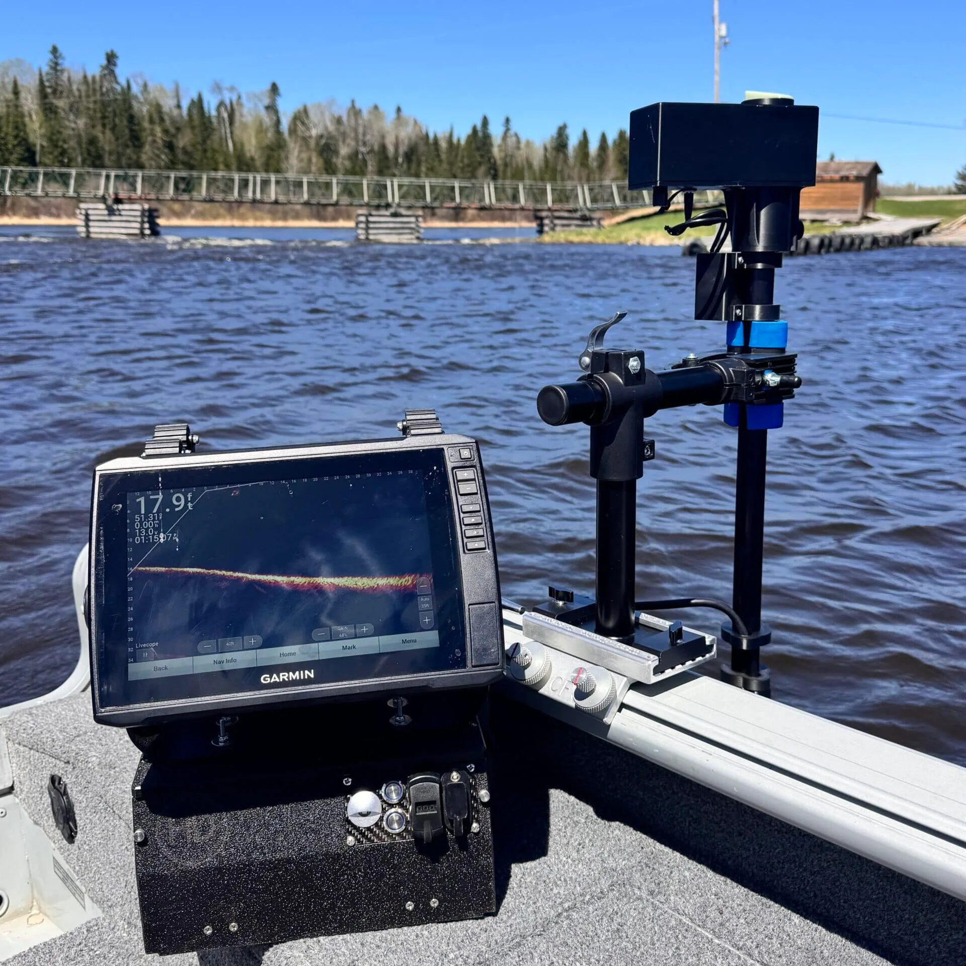 The Wireless Transducer Pole - First Mate XT, with attached camera or sonar, is installed on a small boat floating on choppy water under a clear blue sky with a forested shoreline in the background.
