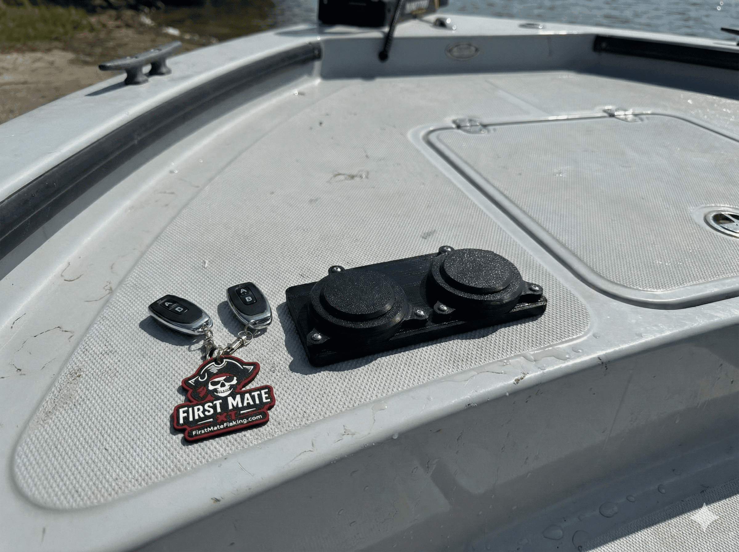 A close-up of a boats deck shows two key fobs, a First Mate keychain with a skull logo, and a black dual-cap device, with water and shoreline visible in the background.