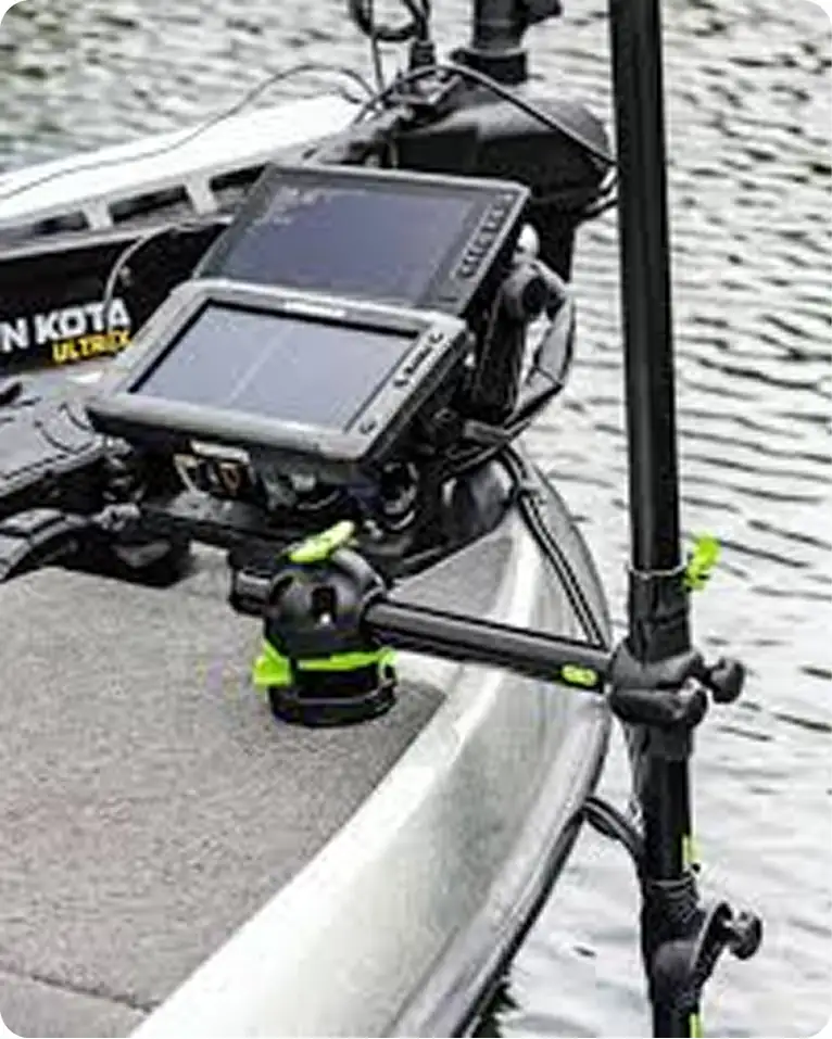 A close-up of a fishfinder and sonar mount attached to the deck of a boat near the water, featuring electronic screens and adjustable arms for positioning.