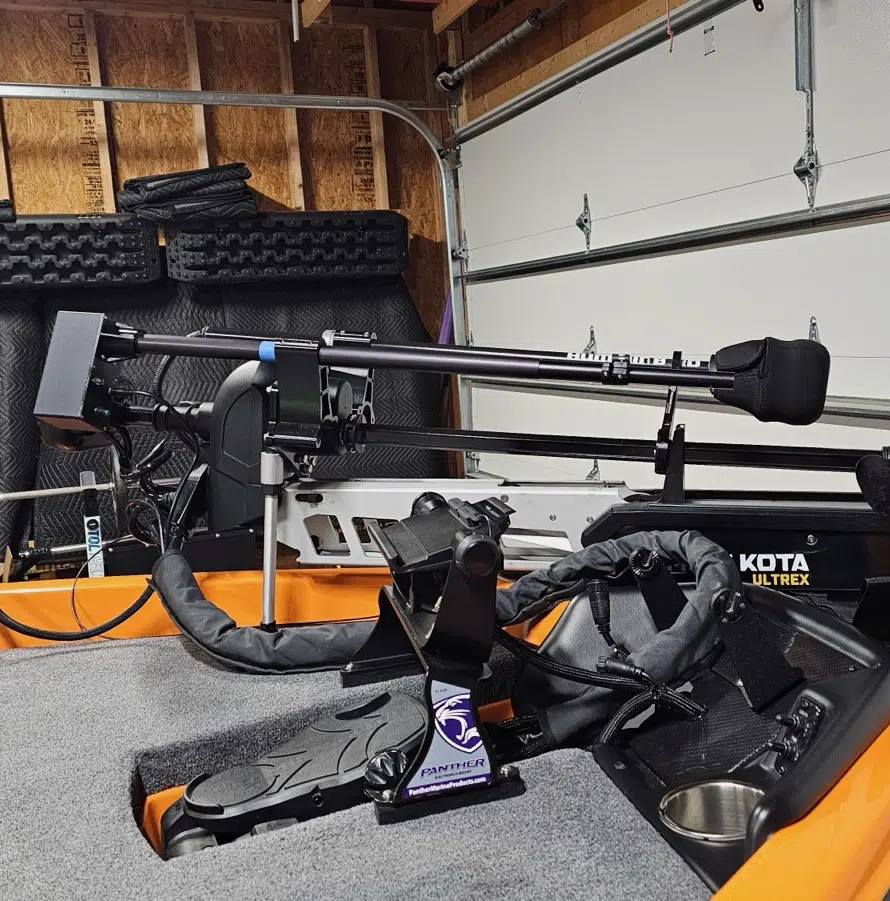 A close-up view of a trolling motor mounted on an orange boat inside a garage, with various boating equipment and accessories visible in the background.